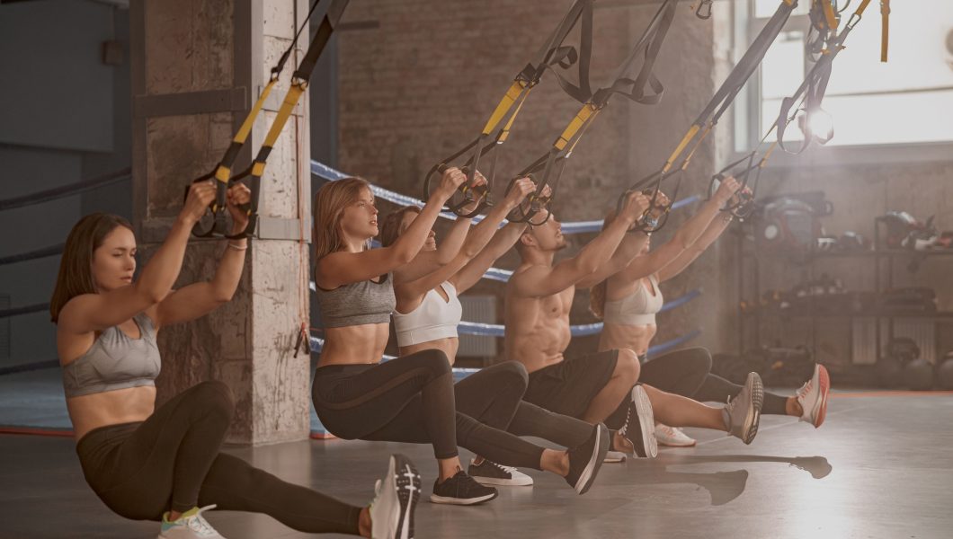 Group of young fitness people using fitness straps in sports club