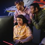 Interracial team standing near gamer playing video game on computer in cyber club