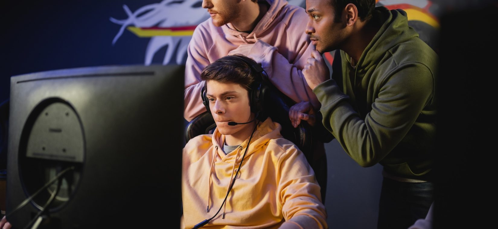 Interracial team standing near gamer playing video game on computer in cyber club